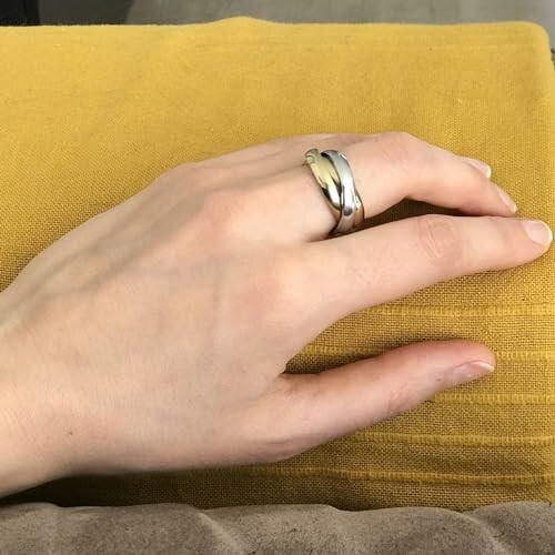 Main avec une bague en argent sur un coussin jaune.