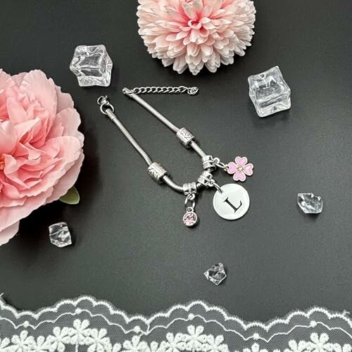 Bracelet en argent avec breloques et fleurs roses sur fond noir.